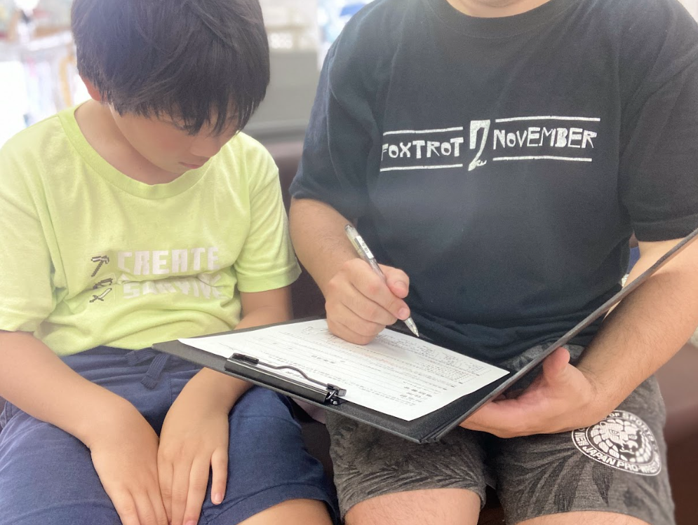 子どもと親が一緒に問診票を記入している様子。整骨院の受付または問診エリアで、リラックスした雰囲気の中、丁寧に記入しているシーン。