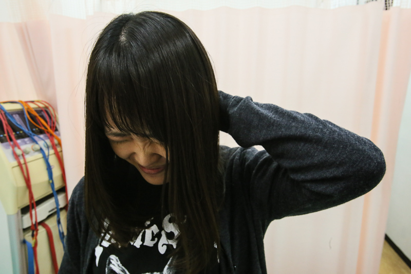 首の痛みを訴えている女性のイメージ画像。首に手を当て、不快感や緊張を感じている様子が表現されている。